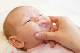 Photo of adult fingers toughing a baby's face. Thumb and middle finger are placed on cheeks.