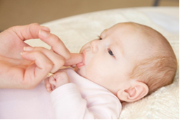 Photo of an adult with a finger placed in a baby's mouth. The finger is placed in the baby's upper jaw.