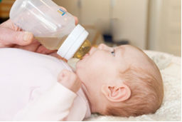Photo of adult giving baby bottle food.