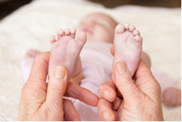 Photo of an adult holding a baby's feet and pressuring it underneath the feet