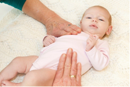 Photo of adult with fingertips on a baby's stomach, swiping towards respectively hip and shoulder