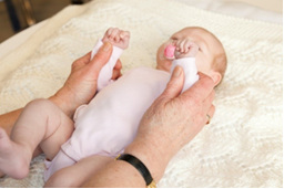 Photo of adult holding a baby's arms, preparing to guide the hands to touching the baby's mouth