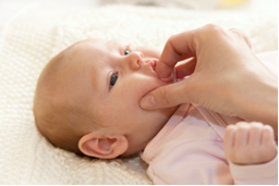 Photo of an adult with a finger in a baby's mouth. Index finger is in the mouth, and ring and little finger are placed outside and under the mouth.
