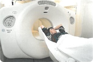 Foto af en PET-CT-skanner, hvor en patient ligger på et fladt leje med armene over hovedet, klar til at blive kørt ind i skannerens hul. Hullet ser ud til at være knap 1 meter i diameter.