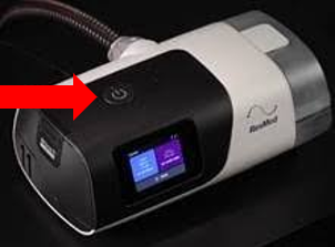CPAP-apparatet og en rød pil der indikere hvor oven på apparatet tænd/sluk knappen befinder sig. Knappen er rund og placeret øverst på apparatet.