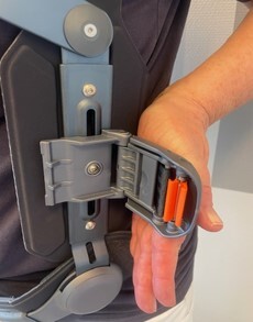 Billedet viser en klap-sp&aelig;nde i siden p&aring; korsettet. Sp&aelig;ndet kan lukkes ved at skubbe fremad med h&aring;nden.